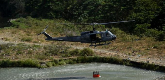Un helicóptero de la Fuerza Aérea desciende en un río para tomar agua en un balde, para ser utilizada en la extinción de un incendio.