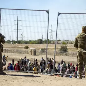 Migrantes esperan junto a una valla fronteriza mientras son vigilados por miembros de la Guardia Nacional de Texas, para ingresar a El Paso, Texas, ayer.