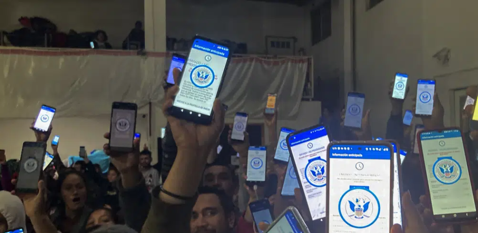 Decenas de migrantes muestran sus teléfonos el domingo 22 de enero de 2023 mostrando en ellos la app CBPOne, en un albergue en Tijuana, México. La aplicación de teléfono móvil para que los inmigrantes busquen asilo en Estados Unidos ha estado sobresaturada desde que se presentó este mes en uno de varios cambios importantes en la respuesta del gobierno estadounidense a flujos migratorios sin precedentes. Los migrantes se sienten cada vez más frustrados por una variedad de mensajes de error en la app. (AP Foto//Elliot Spagat
