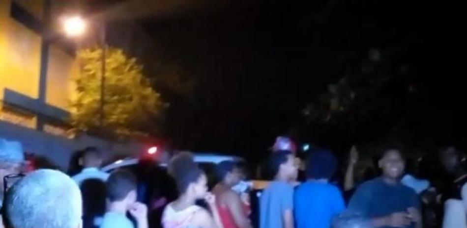 Decenas de personas, autoridades policiales y curiosos, en la escena donde se encontraron los cadáveres en Los Alcarrizos. Captura de video, Listín Diario.
