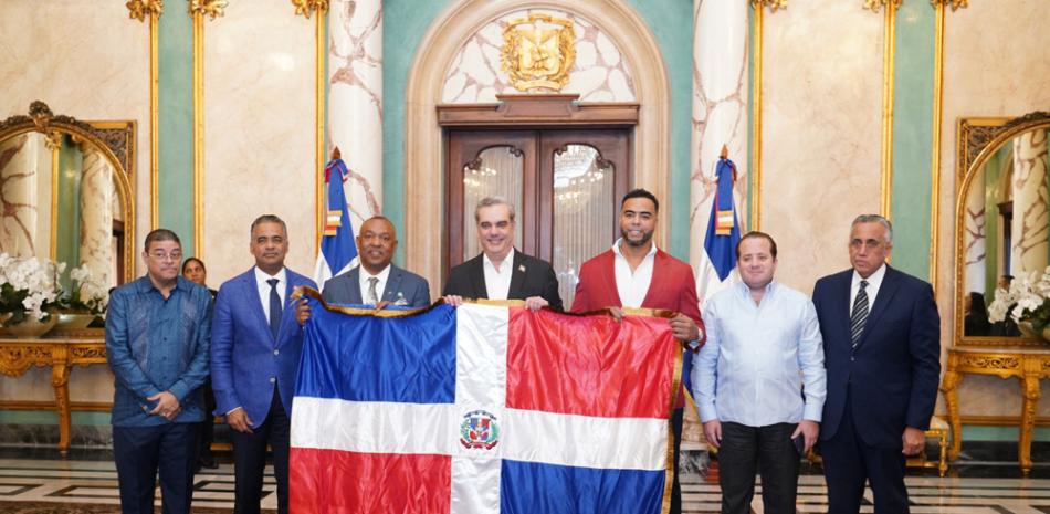 El presidente Luis Abinader entrega la bandera nacional que exhibirá el equipo dominicano a Juan Núñez y a Nelson Cruz, jugador y gerente general. Figuran Francisco Camacho, Joel Santos, José Ignacio Paliza y Luis Mejía Oviedo.
