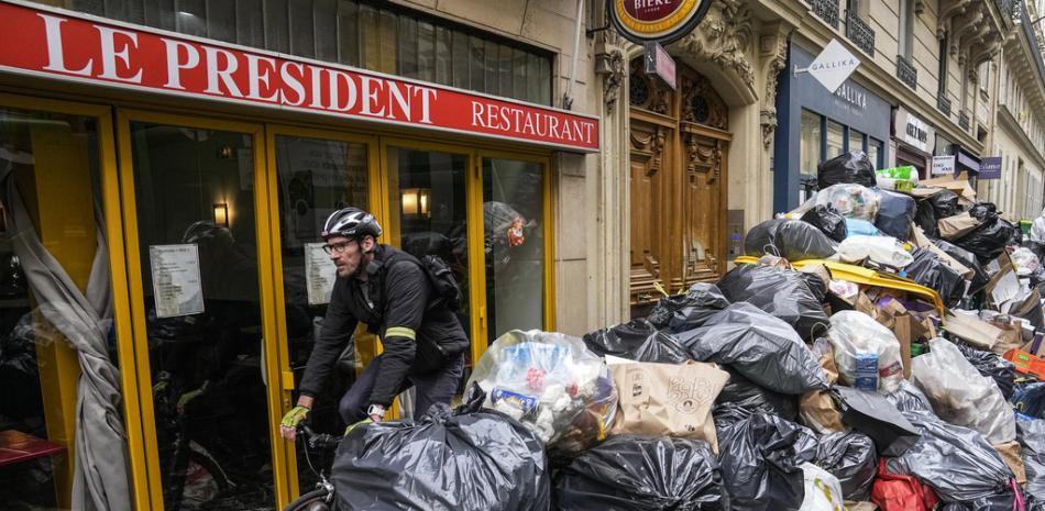 Un ciclista pasa frente a una pila de basura no recolectada junto al café "The President" en París, el martes 21 de marzo de 2023.