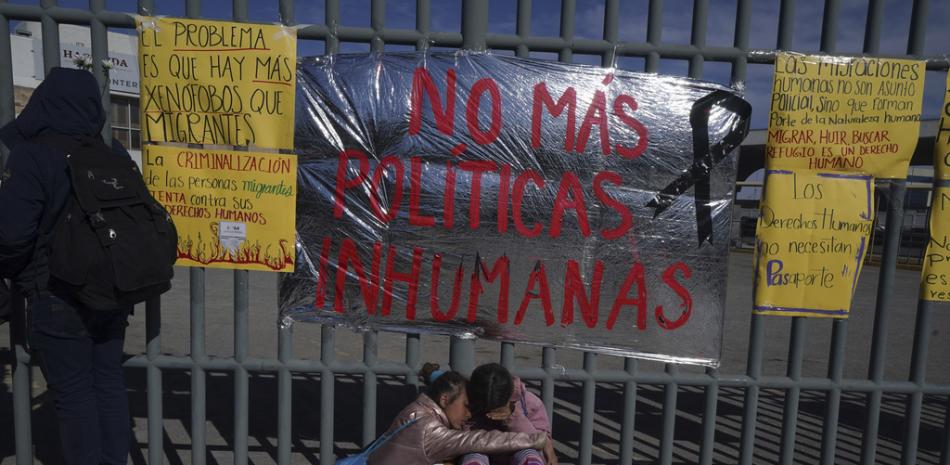 Dos hermanas venezolanas se consuelan sentadas en una vereda ante un centro de detención de migrantes donde docenas de migrantes que temían ser deportado prendieron fuego a las colchonetas, lo que provocó un incendio que mató a docenas de personas, en Ciudad Juárez, México, el martes 28 de marzo de 2023. El cartel dice "No más políticas inhumanas". (AP Foto/Fernando Llano)