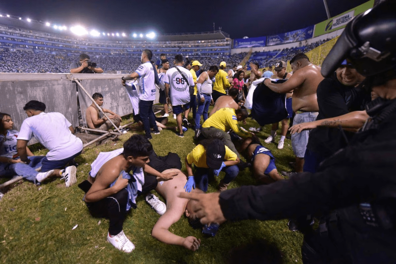 Varios aficionados tratan de ayudar a personas heridas tras la estampida en el Estadio Cuscatlán de El Salvador, donde han muerto al menos 12 personas.