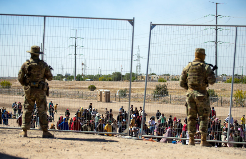 Gran cantidad de migrantes aguardan el miércoles 10 de mayo de 2023 junto a la cerca fronteriza para entrar en El Paso, Texas, ante la mirada de miembros de la Guardia Nacional del estado.